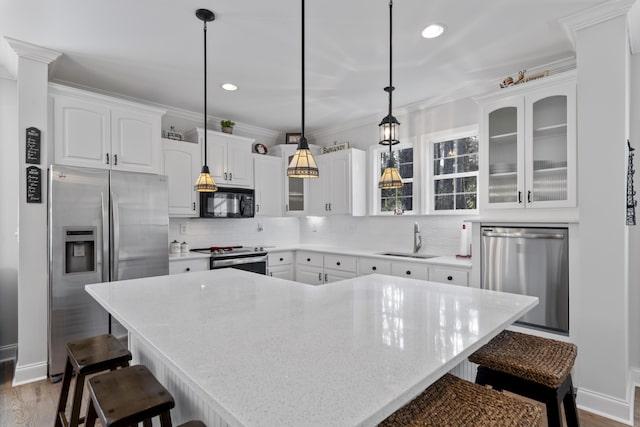 kitchen with appliances with stainless steel finishes, white cabinetry, sink, hanging light fixtures, and a center island