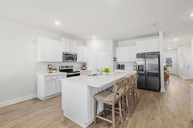 kitchen featuring light hardwood / wood-style floors, white cabinetry, sink, stainless steel appliances, and a center island with sink