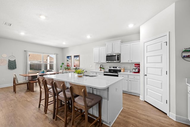 kitchen featuring a center island with sink, white cabinetry, a kitchen bar, and appliances with stainless steel finishes