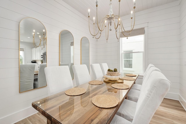 dining area with light wood-type flooring, wooden walls, and an inviting chandelier