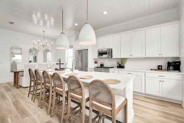 kitchen with pendant lighting, white cabinets, a center island with sink, light hardwood / wood-style floors, and stainless steel appliances