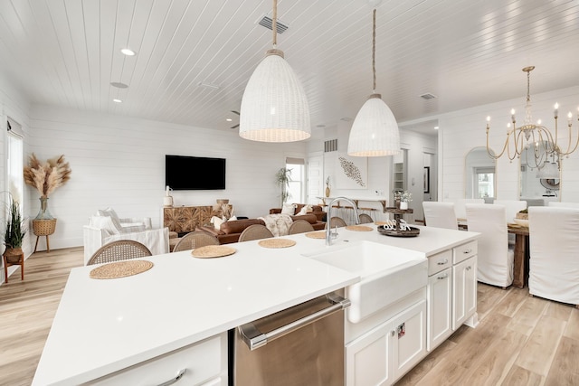 kitchen featuring dishwasher, white cabinetry, hanging light fixtures, light wood-type flooring, and a center island with sink