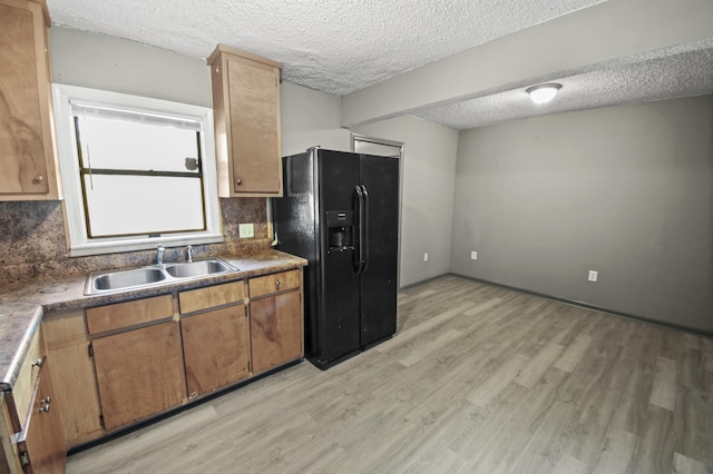 kitchen with sink, light hardwood / wood-style floors, a textured ceiling, black fridge, and decorative backsplash