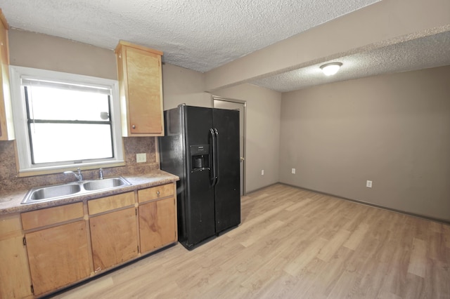 kitchen featuring light wood-style flooring, backsplash, a textured ceiling, black fridge, and a sink