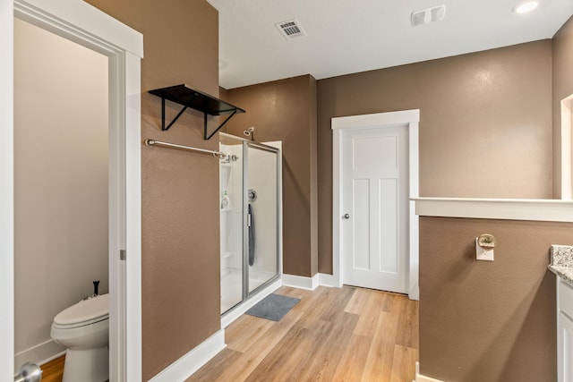 bathroom with hardwood / wood-style floors, toilet, a shower with door, and vanity