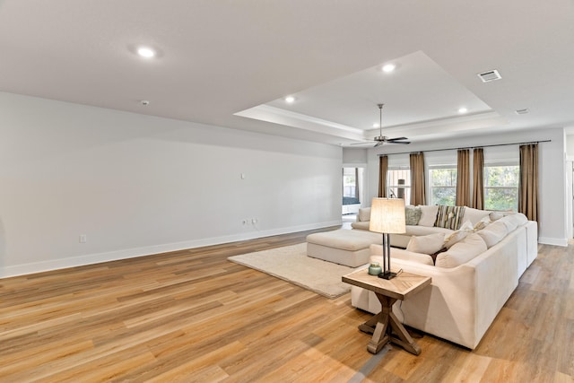 living room featuring light hardwood / wood-style floors, ceiling fan, and a raised ceiling