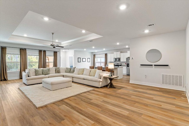 living room with ceiling fan, light hardwood / wood-style floors, and a tray ceiling