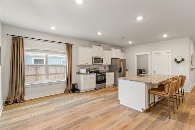 kitchen with appliances with stainless steel finishes, light wood-type flooring, white cabinetry, a kitchen bar, and an island with sink