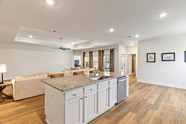 kitchen featuring white cabinets, an island with sink, sink, stainless steel dishwasher, and light hardwood / wood-style flooring