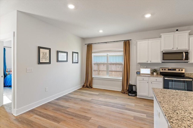 kitchen featuring light wood-type flooring, stainless steel appliances, white cabinetry, and light stone counters