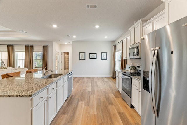 kitchen with light stone countertops, a kitchen island with sink, white cabinets, sink, and stainless steel appliances