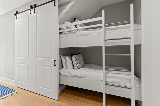 bedroom with wood-type flooring, a barn door, and vaulted ceiling