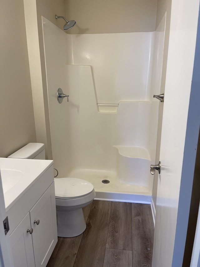 bathroom with wood-type flooring, vanity, walk in shower, and toilet