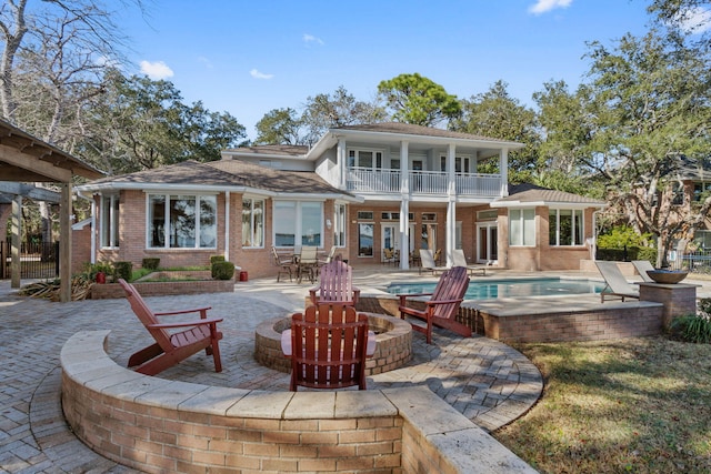 back of property featuring brick siding, an outdoor fire pit, a patio area, a balcony, and an outdoor pool