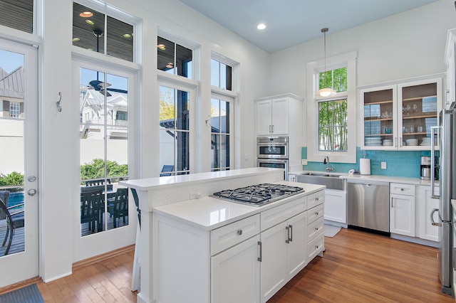 kitchen with appliances with stainless steel finishes, white cabinetry, sink, backsplash, and hanging light fixtures