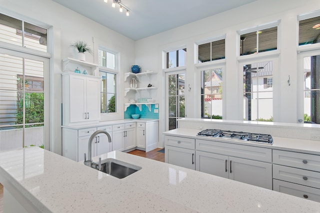 kitchen with sink, backsplash, light stone counters, white cabinets, and stainless steel gas stovetop