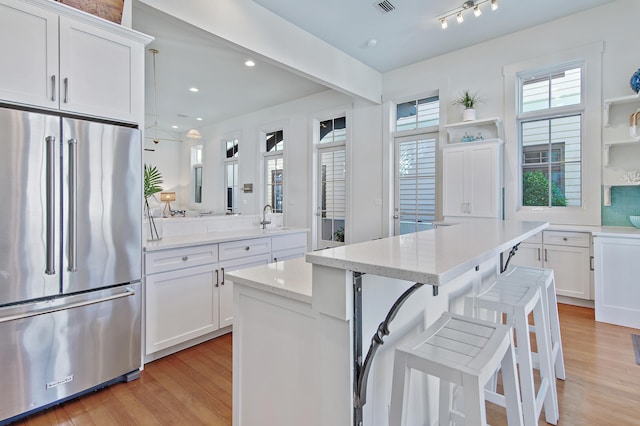 kitchen featuring a breakfast bar area, white cabinetry, high quality fridge, light stone countertops, and backsplash