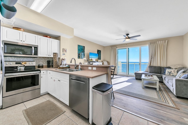 kitchen featuring kitchen peninsula, light tile patterned flooring, white cabinets, and appliances with stainless steel finishes