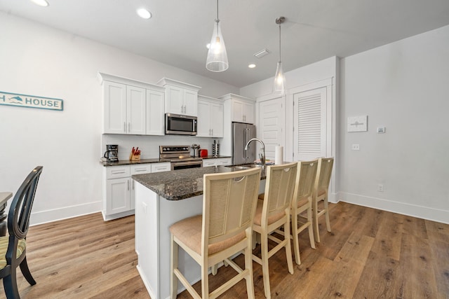 kitchen featuring appliances with stainless steel finishes, a kitchen bar, decorative light fixtures, white cabinetry, and sink