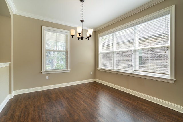 spare room with an inviting chandelier, a wealth of natural light, ornamental molding, and dark hardwood / wood-style flooring