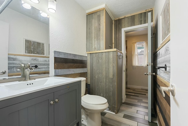 bathroom featuring a textured ceiling, toilet, vanity, and wood walls