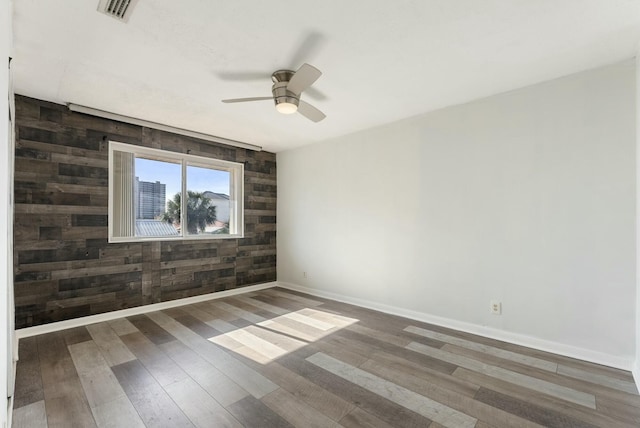 unfurnished room with wood walls, dark wood-type flooring, and ceiling fan