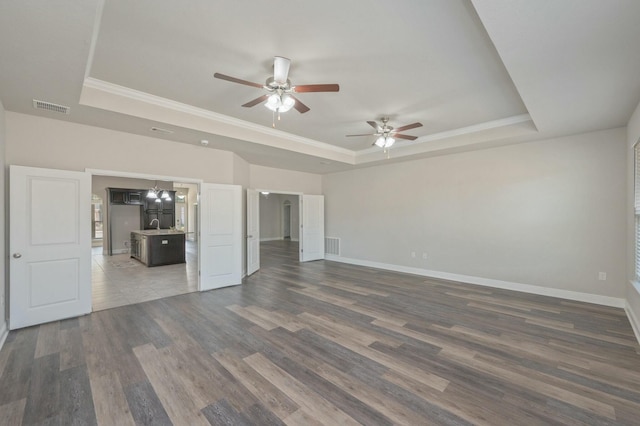 unfurnished living room with dark wood-type flooring, crown molding, and a raised ceiling