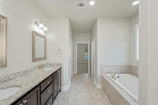 bathroom featuring tile patterned flooring, vanity, and tiled bath