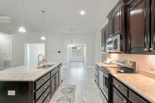 kitchen with pendant lighting, sink, appliances with stainless steel finishes, light stone counters, and an island with sink