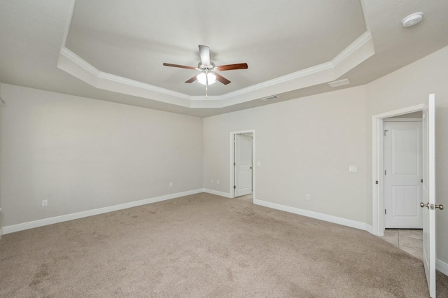 spare room featuring a raised ceiling, ornamental molding, light colored carpet, and ceiling fan