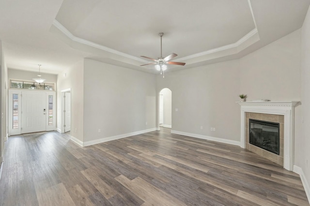 unfurnished living room featuring a tiled fireplace, dark wood-type flooring, a raised ceiling, and ceiling fan