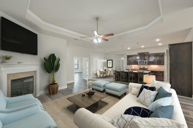 living room with ornamental molding, light hardwood / wood-style flooring, a tile fireplace, and a raised ceiling