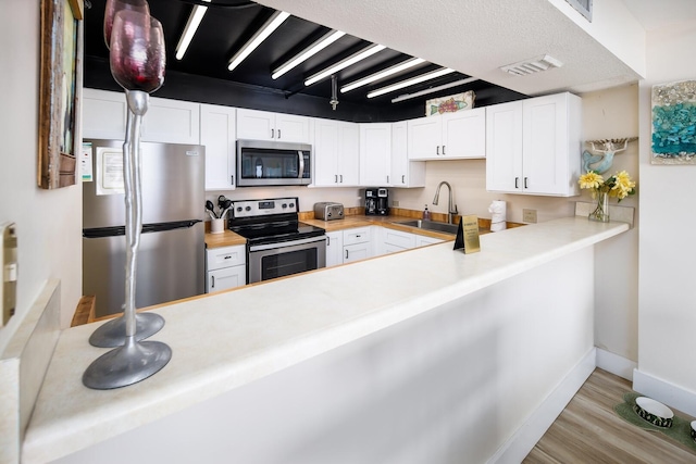 kitchen with sink, appliances with stainless steel finishes, light hardwood / wood-style floors, white cabinets, and wood counters