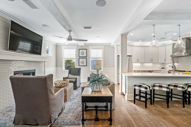 living room featuring a fireplace, light hardwood / wood-style flooring, ceiling fan, and ornamental molding