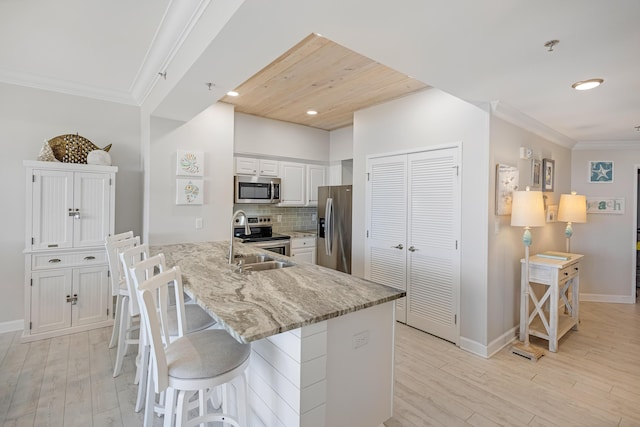 kitchen with a kitchen bar, appliances with stainless steel finishes, white cabinets, light stone countertops, and backsplash