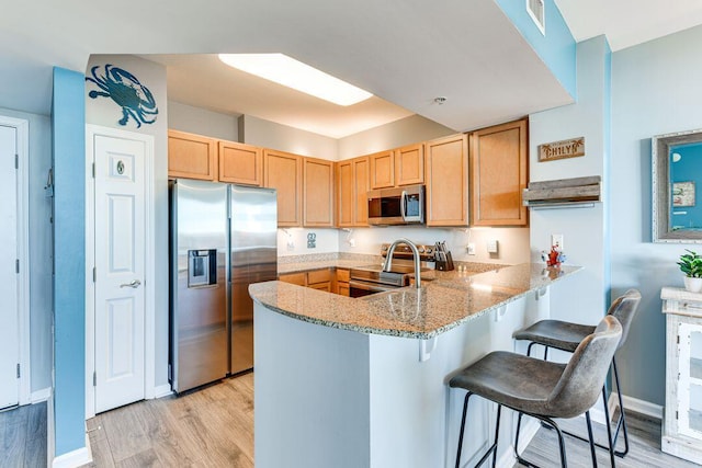 kitchen featuring appliances with stainless steel finishes, light wood-type flooring, kitchen peninsula, a breakfast bar, and light stone counters