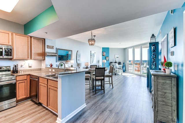 kitchen featuring kitchen peninsula, appliances with stainless steel finishes, sink, a wall of windows, and light hardwood / wood-style floors