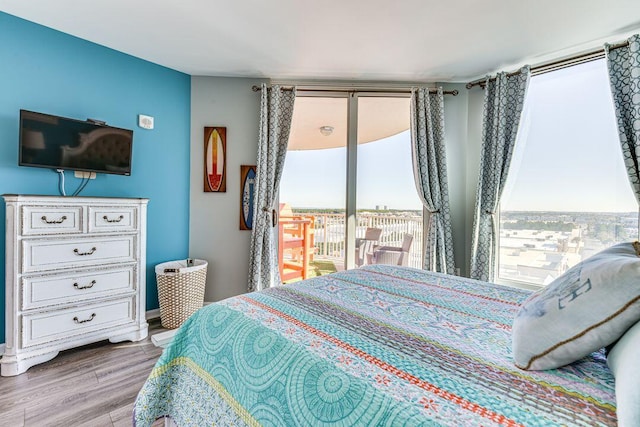 bedroom with wood-type flooring, multiple windows, access to exterior, and expansive windows