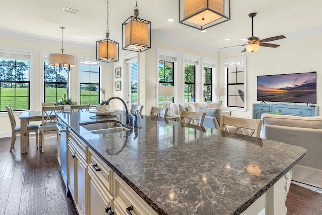 kitchen with sink, a kitchen breakfast bar, a center island with sink, decorative light fixtures, and dark stone counters