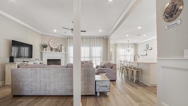 living room featuring sink, ornamental molding, ceiling fan, and light wood-type flooring