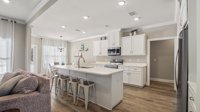 kitchen with pendant lighting, appliances with stainless steel finishes, a kitchen island with sink, and white cabinets