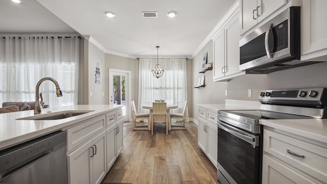 kitchen featuring appliances with stainless steel finishes, white cabinetry, sink, crown molding, and light hardwood / wood-style flooring