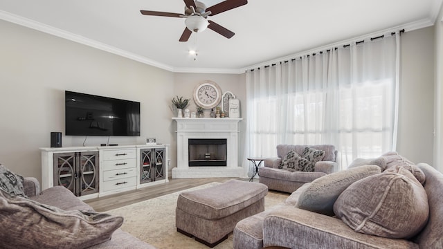 living room with ornamental molding, a brick fireplace, ceiling fan, and light wood-type flooring