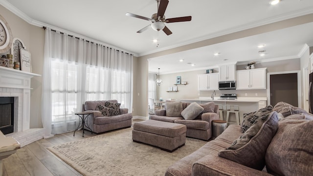 living room with crown molding, ceiling fan, light hardwood / wood-style floors, and a brick fireplace