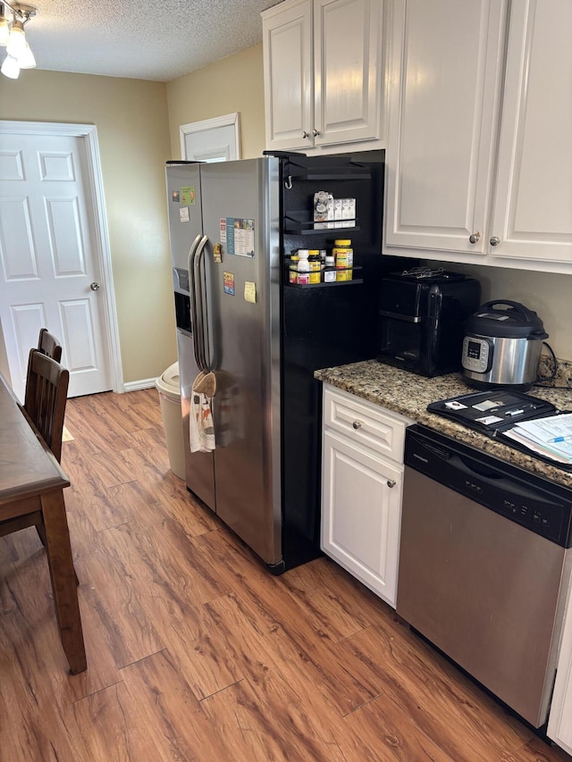 kitchen featuring white cabinetry, a textured ceiling, dark stone counters, stainless steel appliances, and hardwood / wood-style floors