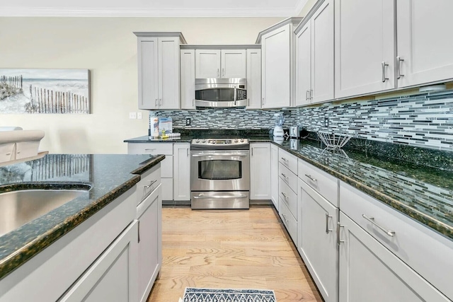 kitchen with backsplash, ornamental molding, appliances with stainless steel finishes, and dark stone counters