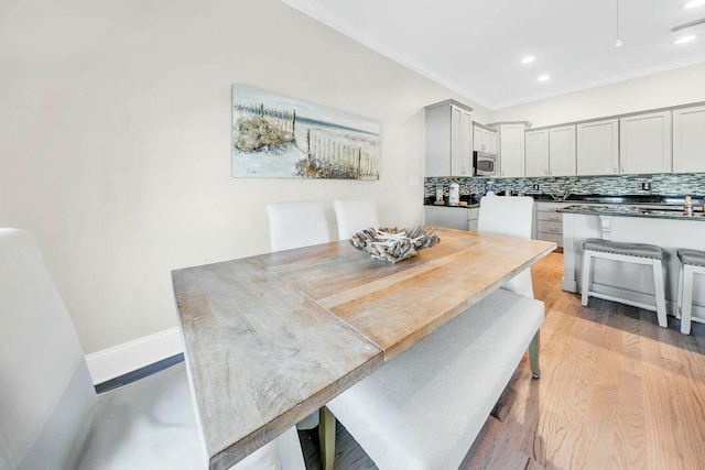 dining space with ornamental molding and light hardwood / wood-style flooring