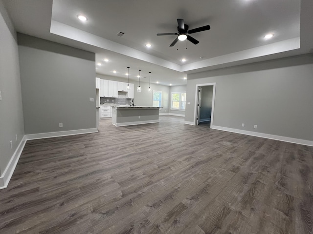 unfurnished living room featuring ceiling fan, sink, dark hardwood / wood-style flooring, and a tray ceiling