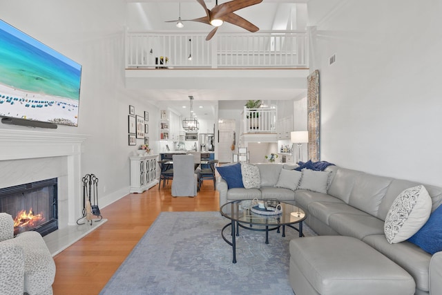 living room with ceiling fan, a high end fireplace, wood-type flooring, and a high ceiling