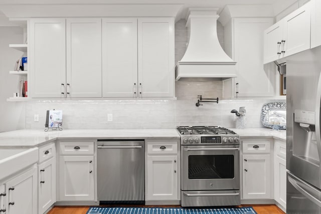 kitchen with appliances with stainless steel finishes, white cabinetry, light stone counters, custom range hood, and decorative backsplash